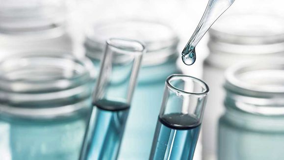 Pipette adding blue fluid test tube close up
