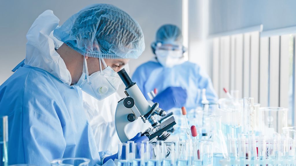 biochemical research scientist team working with microscope for coronavirus vaccine development in pharmaceutical research labolatory
