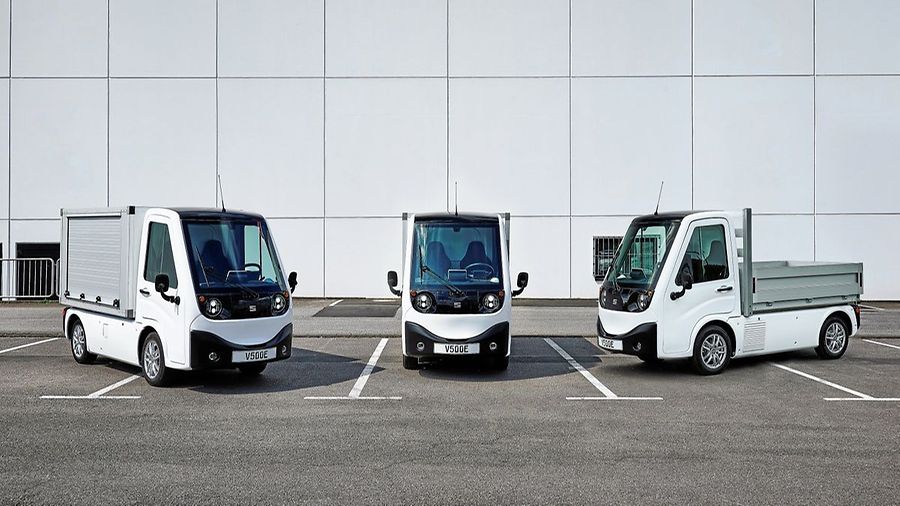 Drei weiße Elektrotransporter auf einem Parkplatz vor einer Hallenfassade: links mit Kofferaufbau, in der Mitte Fahrgestell mit Fahrerhaus, rechts Pritschenvariante.