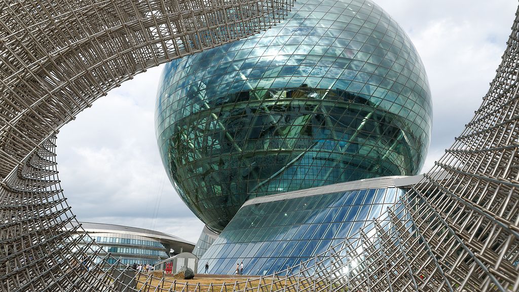 Gläserner Kugelbau des Museum of the Future in Astana, Kasachstan, eingerahmt von einer geschwungenen Metallkonstruktion im Vordergrund.
