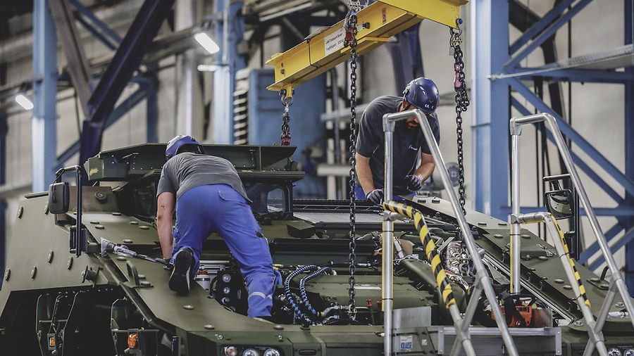 Zwei Männer mit Schutzhelmen arbeiten an einem gepanzerten Fahrzeug