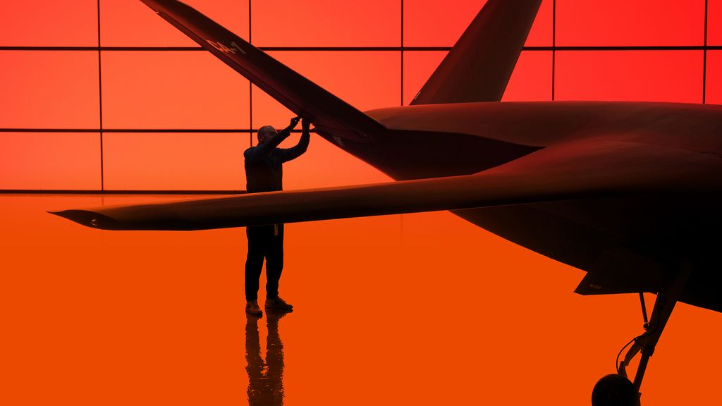 Silhouette einer Person neben einem großen Flugzeug in einer von orange-rotem Licht durchfluteten Halle