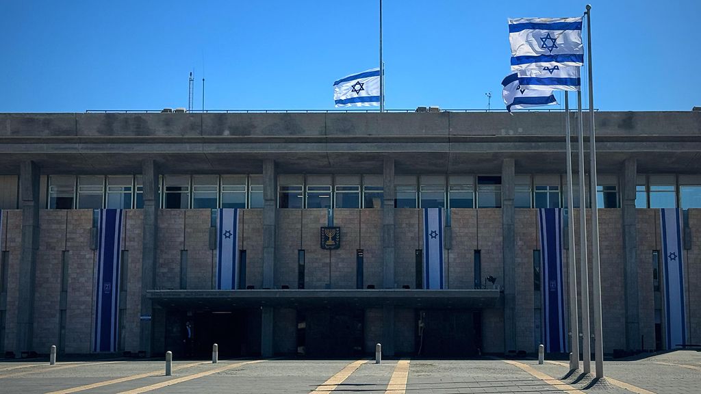 Fontalansicht des israelischen Parlamentsgebäudes Knesset in Jerusalem vor blauem Himmel mit mehreren wehenden israelischen Flaggen 