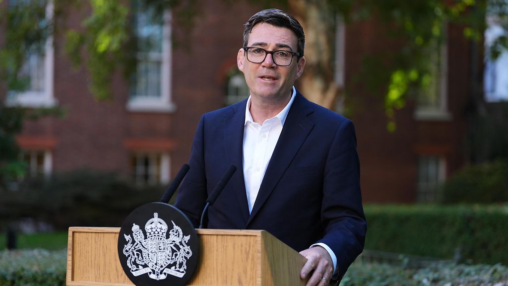 Großbritanniens Premierminister Andy Burnham steht hinter einem Rednerpult und hält eine Rede. Dabei trägt er einen dunkelblauen Anzug mit einem weißen Hemd.