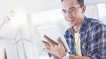 Checking news. Joyful brunette holding tablet in both hands, expressing positivity