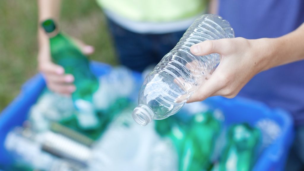 Gruene Flaschen und Metalldosen in einer Recycling Tonne