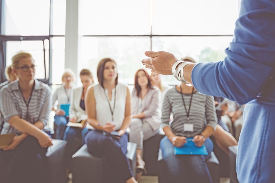Hand of a trainer addressing group of females sitting in a conference hall. Female hand against defocused group of women attending seminar.