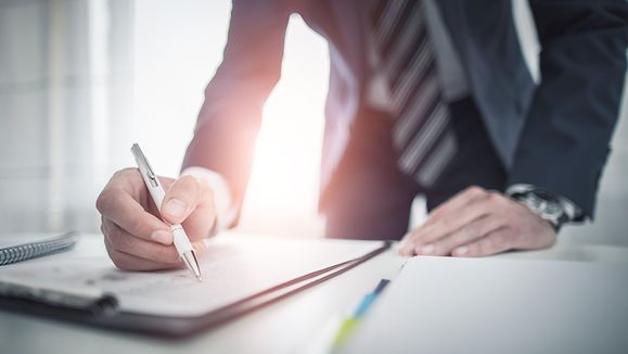 Geschaeftsmann unterzeichnet Vertragsdokument auf dem Schreibtisch und schließt einen Vertrag ab.