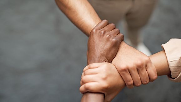 Shot of a group of businesspeople linking arms in solidarity in a modern office.