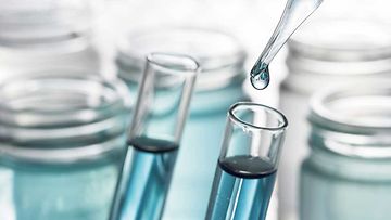 Pipette, die eine blaue Flüssigkeit in ein Teströhrchen tropft
