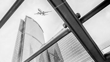 Blick von unten an Hochhäusern hoch zum Himmel auf ein Flugzeug
