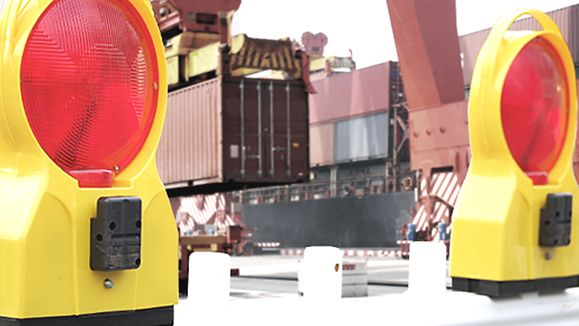Symbolbild Handelsbeschränkungen: Warnleuchten vor Containerterminal